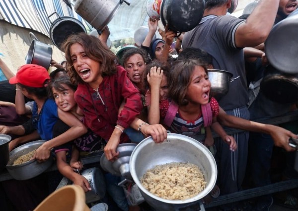 Ii palestinesi si accalcano per ricevere un pasto caldo da una cucina di beneficenza nel campo profughi di Nuseirat, nella Striscia di Gaza assediata da Israele, dove l'ONU ha dichiarato la carestia dopo quasi due anni di guerra
